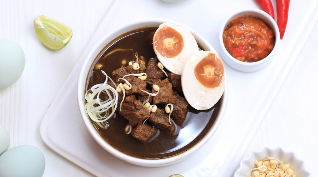Rawon, Indonesian Traditional Beff Black Soup from East Java. Served on a Bowl wth Shrimp Cracker (kerupuk Udang) and Chilli Paste and Salted Egg