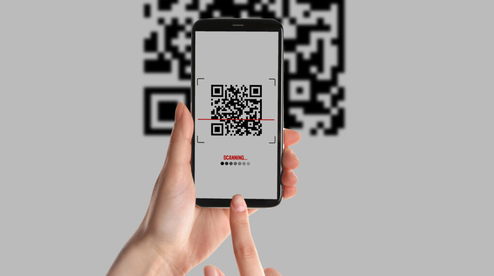 Woman scanning QR code with smartphone on light background, closeup